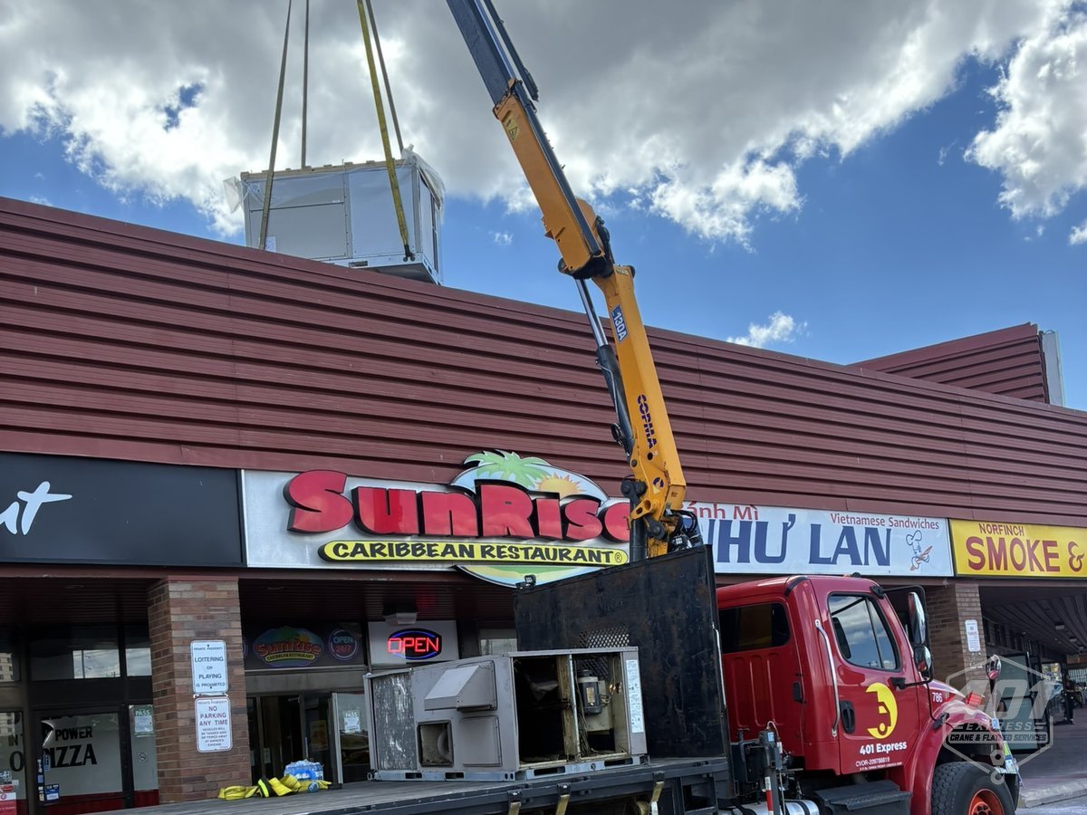 401 Express crane lifting a new rooftop HVAC unit onto a plaza roof in Toronto while the old RTU sits on the flatbed