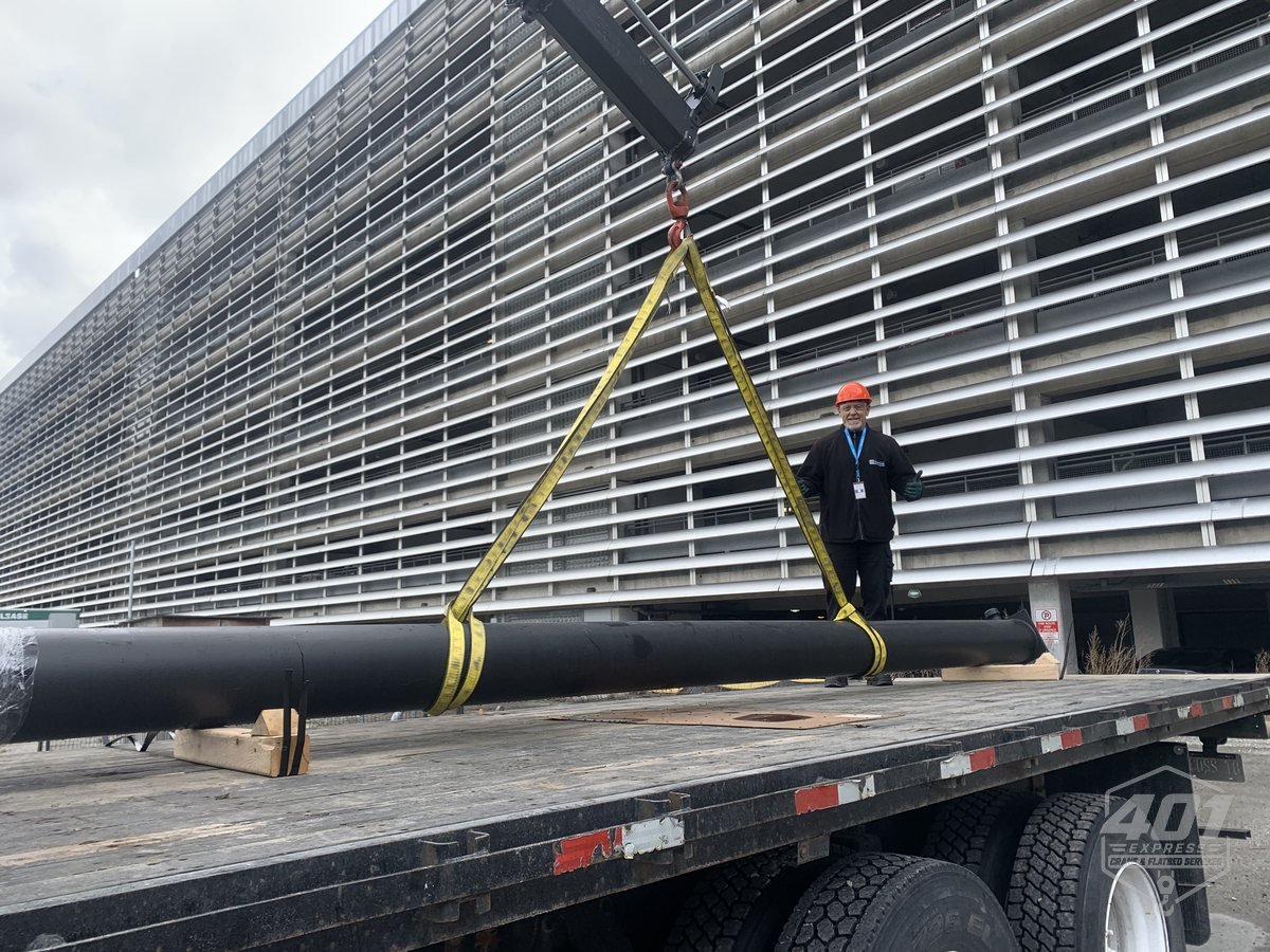 Large steel pipe suspended in yellow slings from the 401 Express crane at a Toronto commercial job site